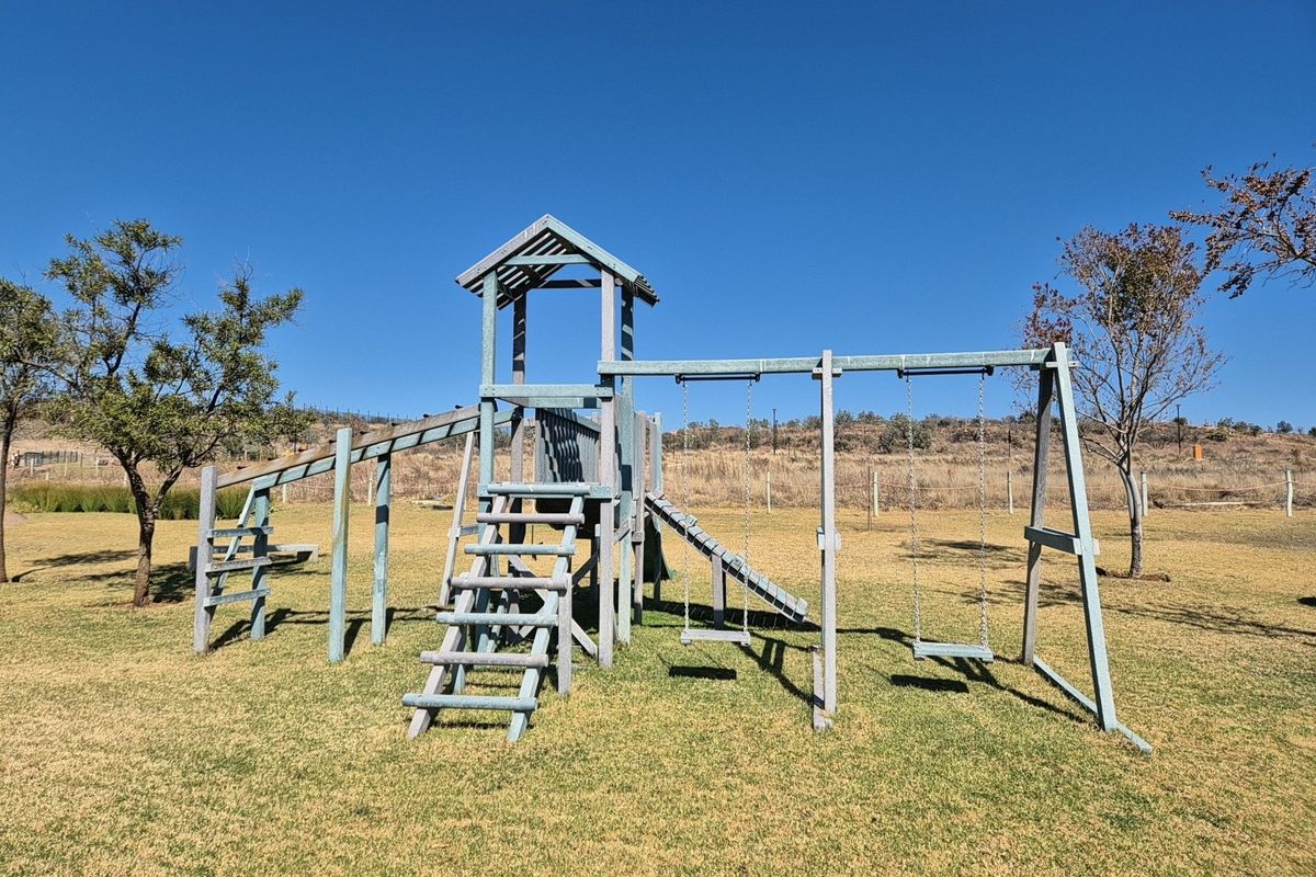 A residential garden featuring a wooden playground structure with swings and a slide set on a maintained lawn.