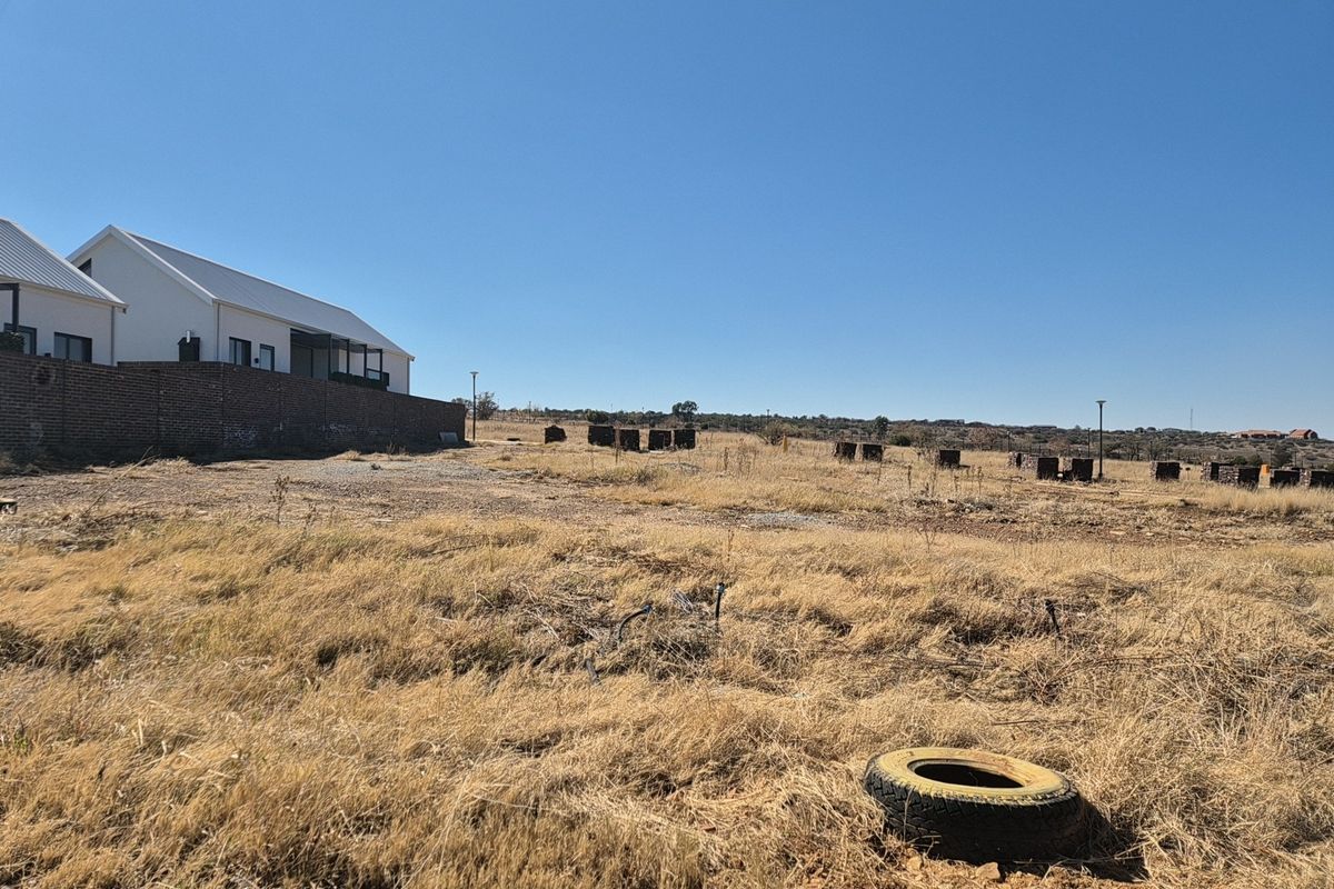 A vacant residential plot featuring dry grass, a brick boundary wall, and existing street lighting infrastructure.