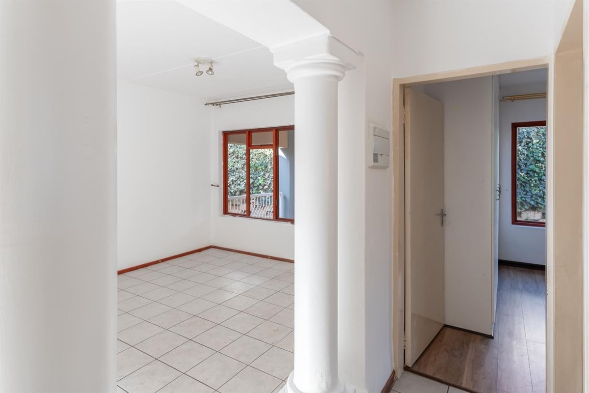 An empty living area featuring tiled flooring, a decorative column, and access to an adjacent room with wood-look flooring.
