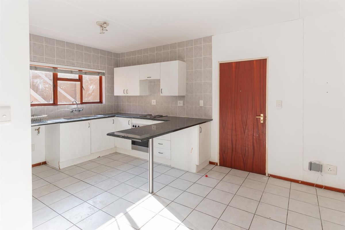 A functional kitchen featuring white cabinetry, dark granite countertops, a built-in oven and hob, and tiled flooring throughout.