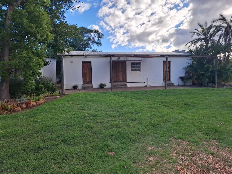 A rear view of a farm dwelling featuring a covered patio area, white exterior walls, and established garden surroundings.