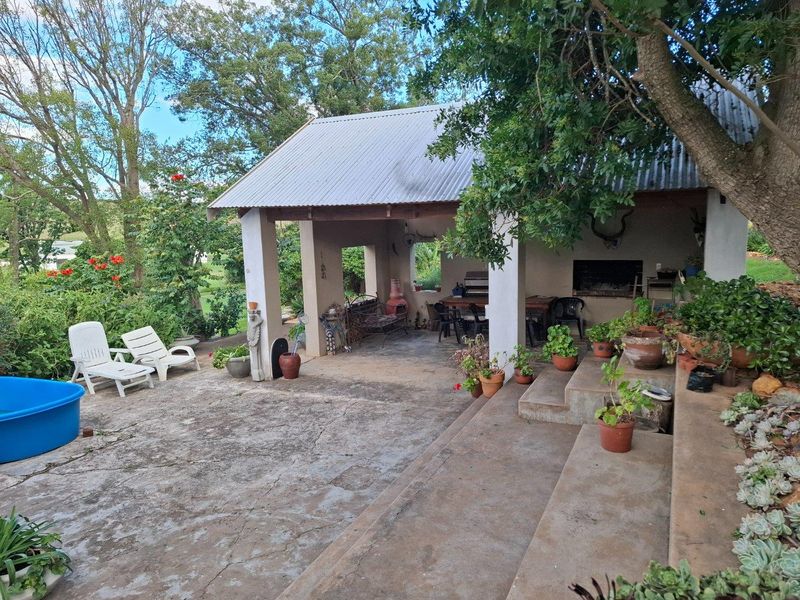 A covered outdoor patio area featuring a built-in braai, concrete flooring, and steps leading to a garden setting.