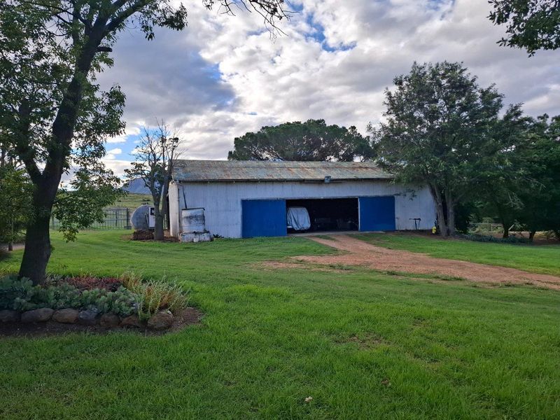 A rustic farm outbuilding featuring corrugated metal construction, large sliding doors, and a spacious surrounding lawn area.