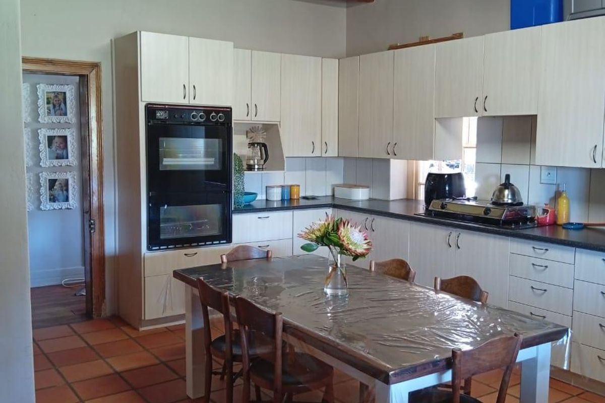 Spacious kitchen featuring light-toned cabinetry, built-in double oven, exposed timber ceiling beams, and terracotta floor tiles, offering a rustic farm-style aesthetic.