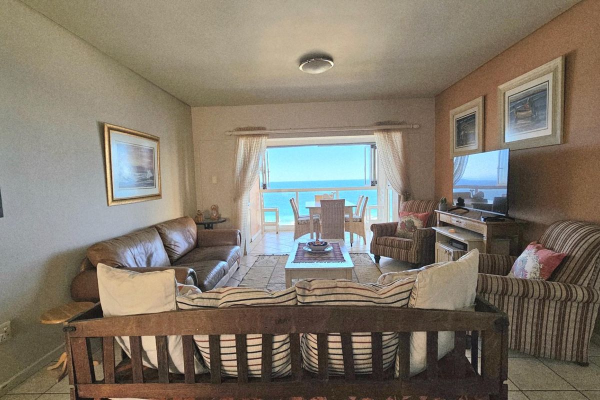 A comfortable living room featuring tiled flooring and large sliding doors that open onto a balcony with expansive ocean views.