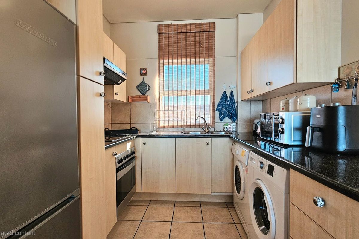 A functional kitchen featuring light wood cabinetry, dark granite countertops, integrated oven and hob, and dedicated space for laundry appliances.