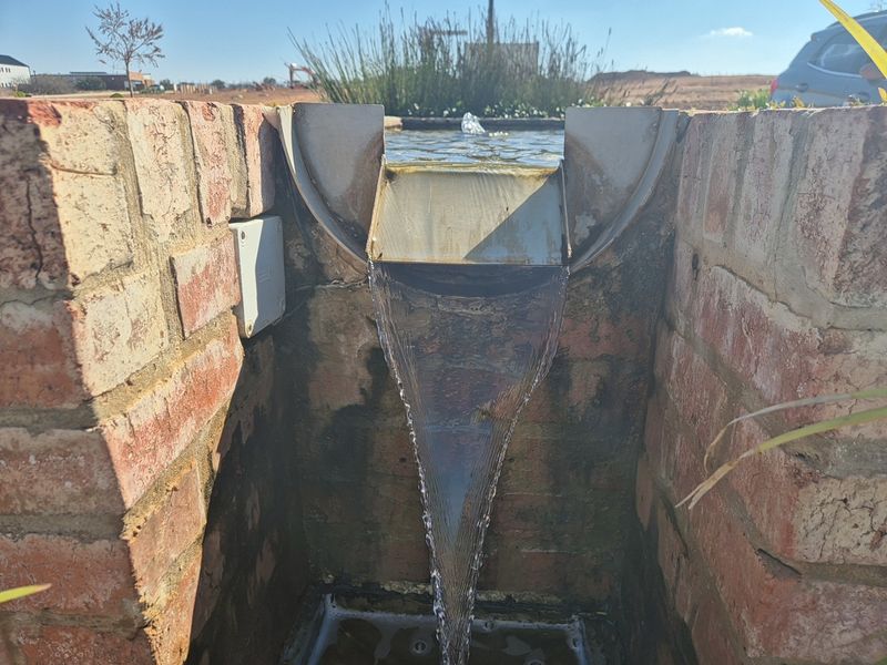 A close-up view of a brick-constructed water feature with a cascading fountain element located within the garden area.