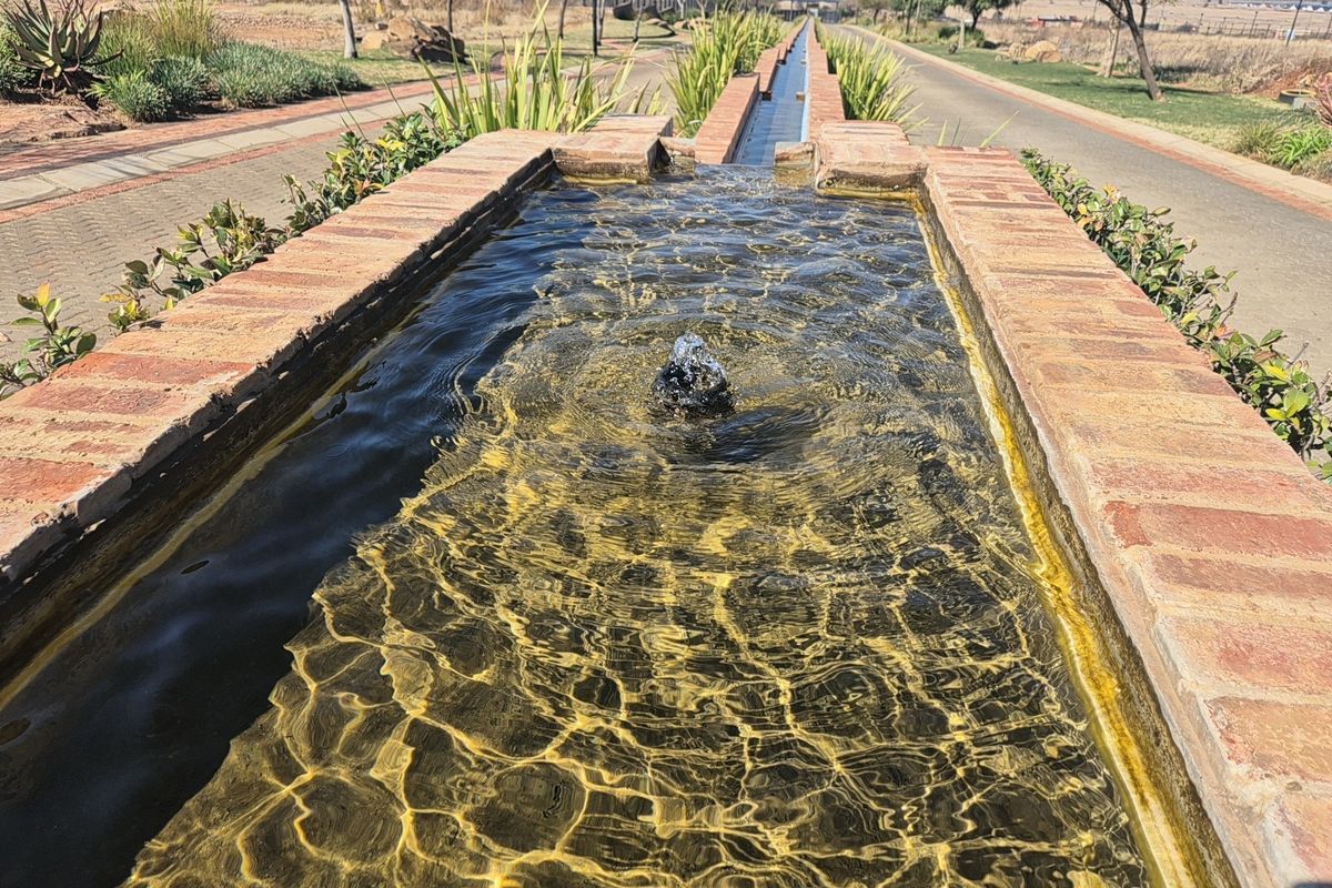 A well-maintained brick-lined water feature and fountain set within a landscaped garden area, providing an attractive aesthetic element to the property grounds.
