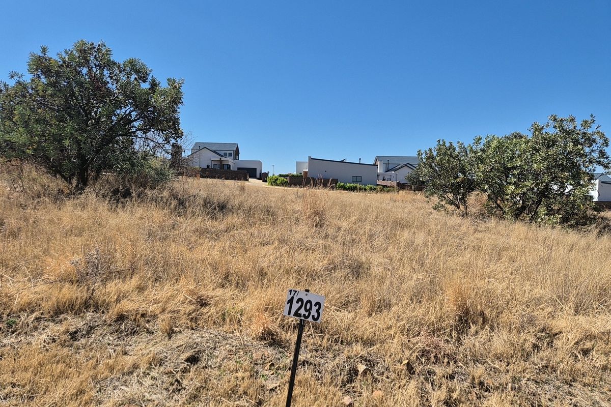 A view of a vacant residential plot featuring dry grass and a gentle slope, situated in a developed neighborhood.