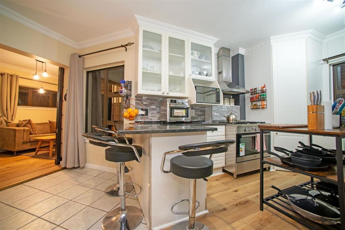 A well-appointed kitchen featuring granite countertops, glass-front cabinetry, a stainless steel extractor fan, and a built-in oven, seamlessly flowing into the adjacent living area.
