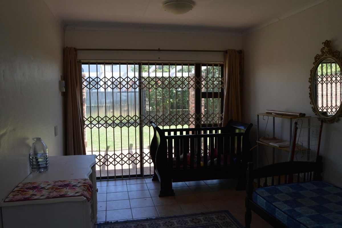 A bedroom featuring tiled flooring and a sliding glass door with a security gate, providing direct access to the rear garden area.