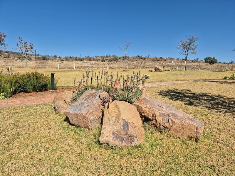 A well-maintained garden area featuring a decorative rock arrangement, brick pathways, and open lawn space within a residential estate setting.