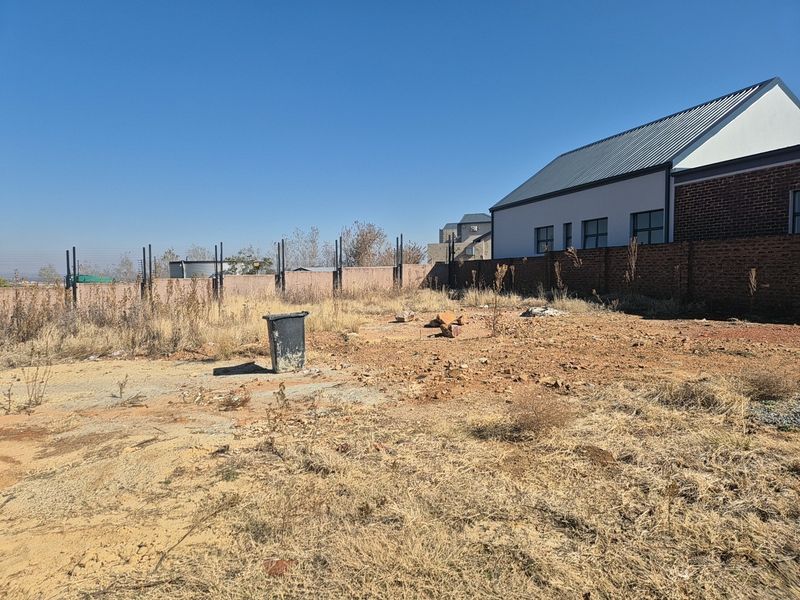 A vacant residential plot featuring perimeter walling with electric fencing, adjacent to an existing modern structure with a metal roof.