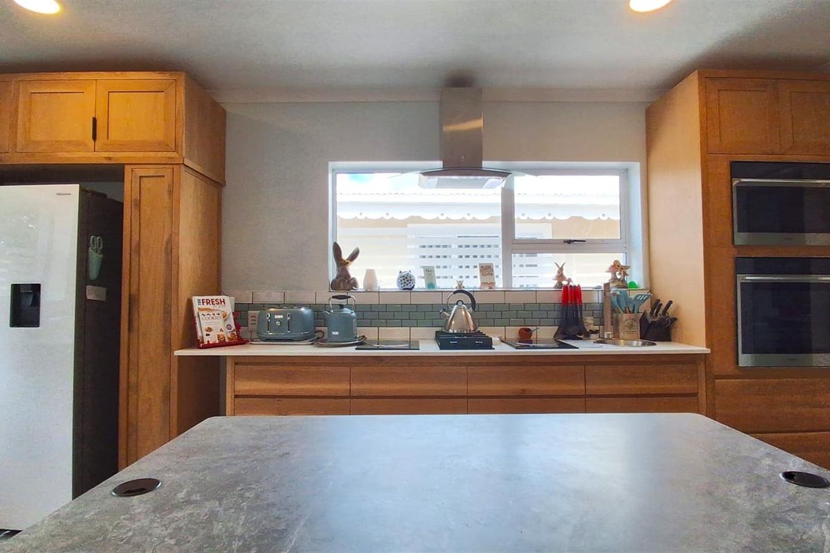 A well-maintained kitchen featuring light wood cabinetry, a built-in double oven, stainless steel extractor fan, and a central island with a stone-look countertop.