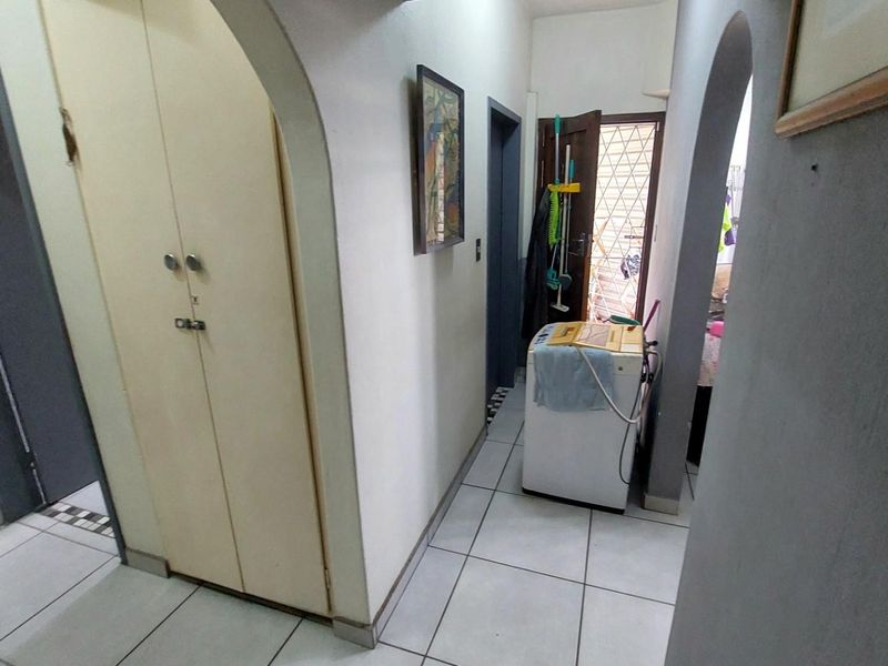 A functional hallway featuring tiled flooring, built-in storage cupboards, and arched architectural details leading to adjacent rooms.