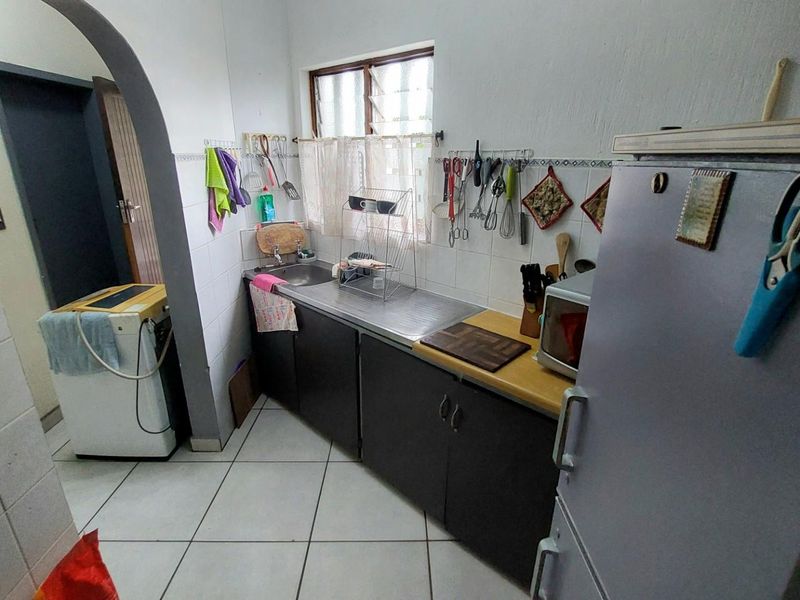 A compact kitchen featuring dark cabinetry, a stainless steel sink, and tiled flooring, with an adjacent utility area visible through an arched doorway.