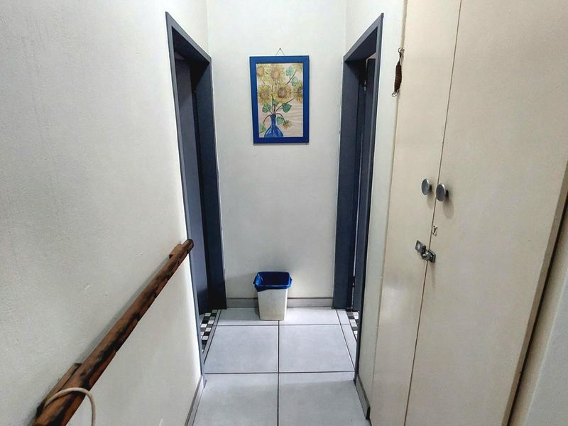 A functional hallway featuring tiled flooring, built-in storage cabinetry, and a wall-mounted handrail providing access to adjacent rooms.