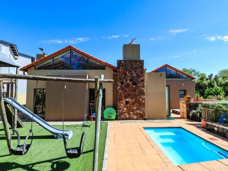 Rear view of the property featuring a swimming pool, paved deck, artificial lawn, and a distinctive stone-clad chimney with large triangular windows.