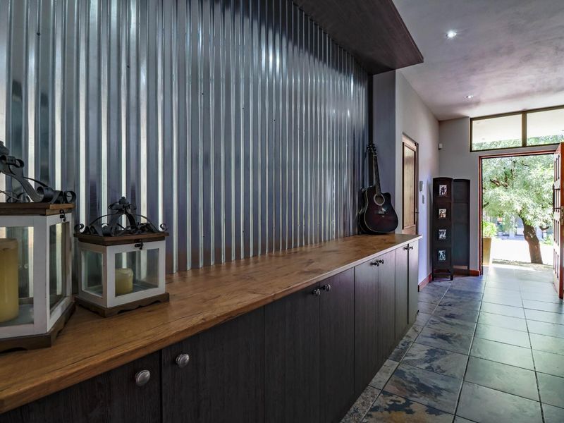 A well-lit hallway featuring unique corrugated metal wall cladding, extensive built-in cabinetry with a wooden countertop, and durable tiled flooring leading to the entrance.