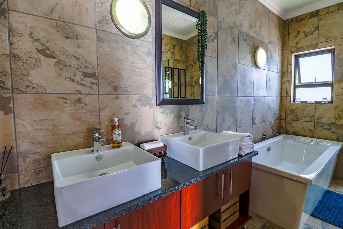 Modern bathroom featuring a double vanity with vessel sinks, stone countertop, built-in bathtub, and full-height wall tiling.