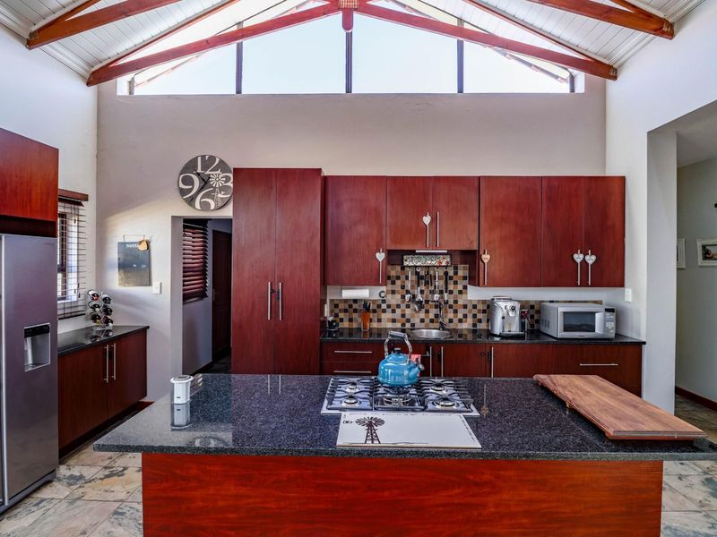 Spacious kitchen featuring dark wood cabinetry, granite countertops, a central island with a gas cooktop, and a high vaulted ceiling with exposed timber beams.