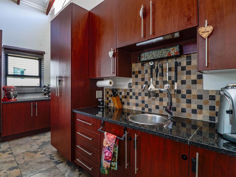 A well-maintained kitchen featuring dark wood cabinetry, granite countertops, a mosaic tiled backsplash, and stone flooring under a vaulted ceiling.