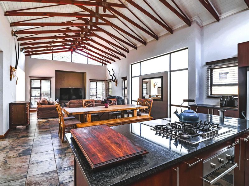Spacious open-plan living and kitchen area featuring high vaulted ceilings with exposed timber trusses, granite countertops, and large windows providing ample natural light.