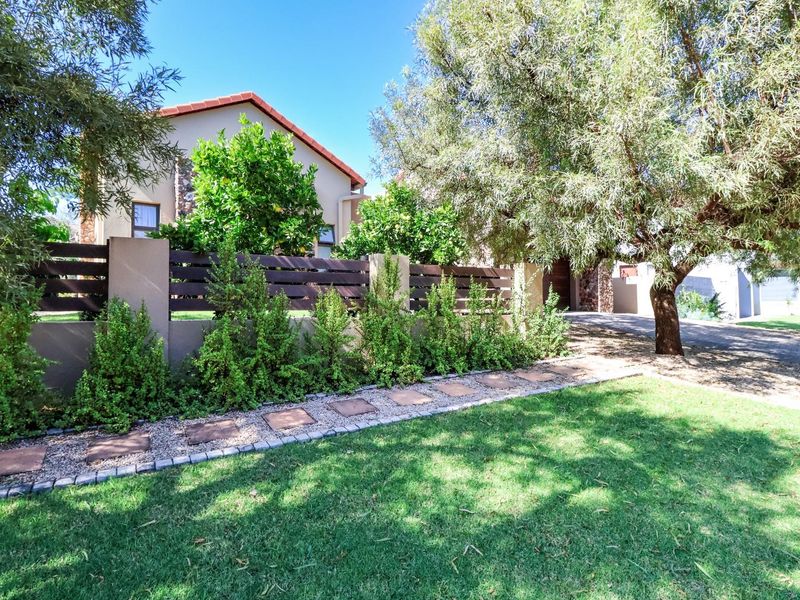 A well-maintained front garden featuring a paved walkway, timber slat fencing with masonry pillars, and mature trees, providing a neat street-facing facade.