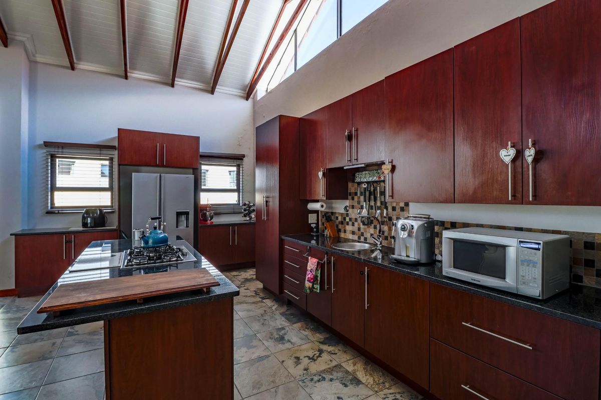 Spacious kitchen featuring dark wood cabinetry, granite countertops, a central island with a gas hob, and a high vaulted ceiling with clerestory windows.
