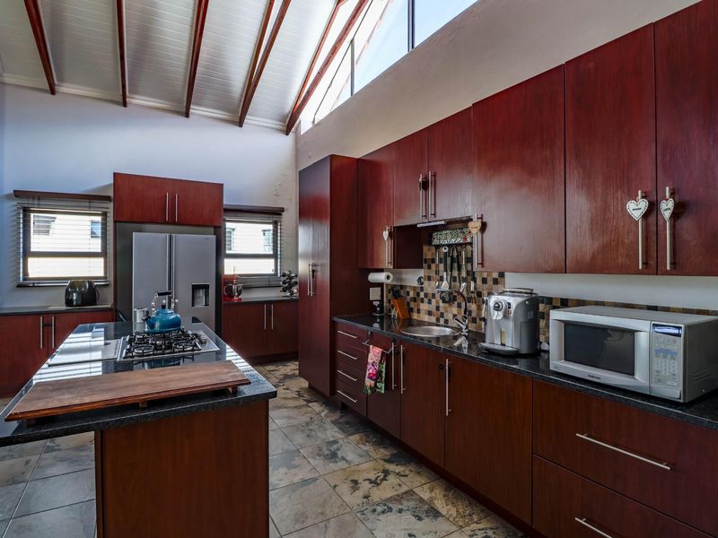 Spacious kitchen featuring dark wood cabinetry, granite countertops, a central island with a gas hob, and a high vaulted ceiling with clerestory windows.