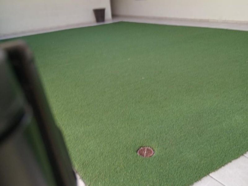 An open-air communal patio area featuring artificial turf, tiled flooring, and perimeter railings within an apartment complex.
