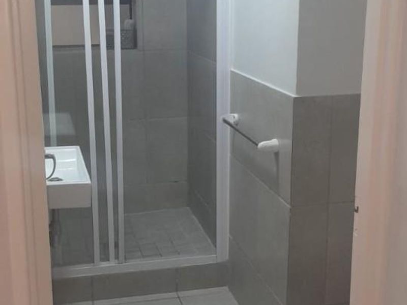 A functional bathroom featuring a shower enclosure, tiled walls and flooring, a washbasin, and a toilet.