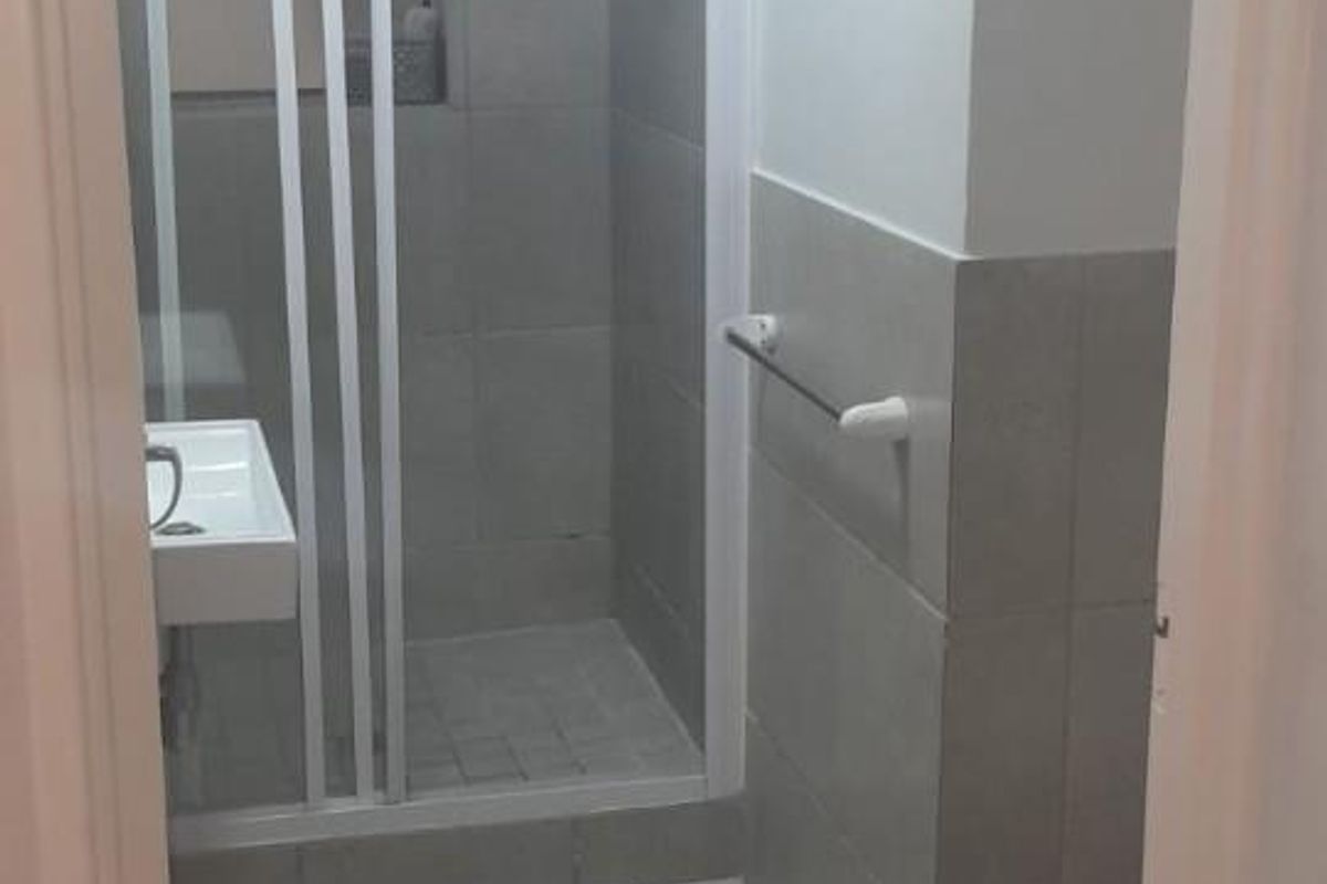 A functional bathroom featuring a shower enclosure, tiled walls and flooring, a washbasin, and a toilet.
