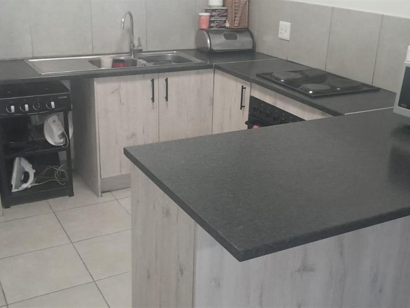 A functional kitchen featuring light wood-look cabinetry, dark laminate countertops, a built-in oven and hob, and tiled flooring.