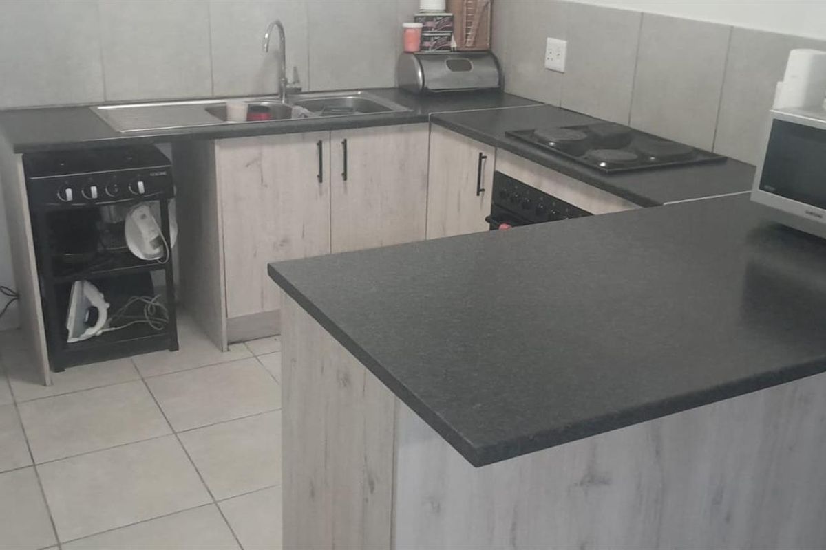 A functional kitchen featuring light wood-look cabinetry, dark laminate countertops, a built-in oven and hob, and tiled flooring.