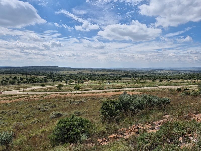 A scenic elevated view of the surrounding natural landscape and estate road infrastructure, showcasing the expansive terrain of the vacant residential land.