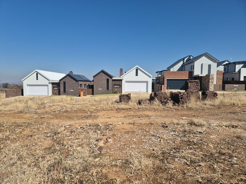 A view of a vacant residential plot situated in a developed estate with modern homes in the background.