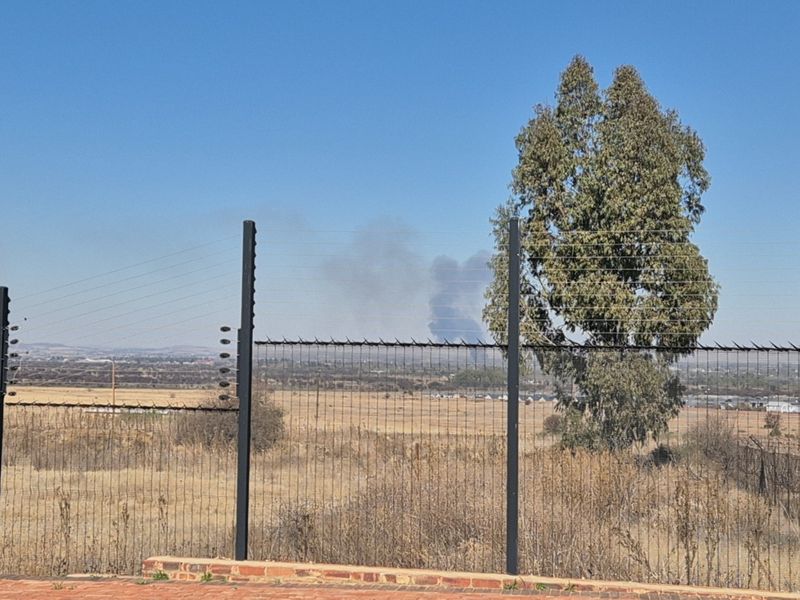 A view overlooking open vacant land, secured by wire mesh and electric fencing, with distant landscape visible.