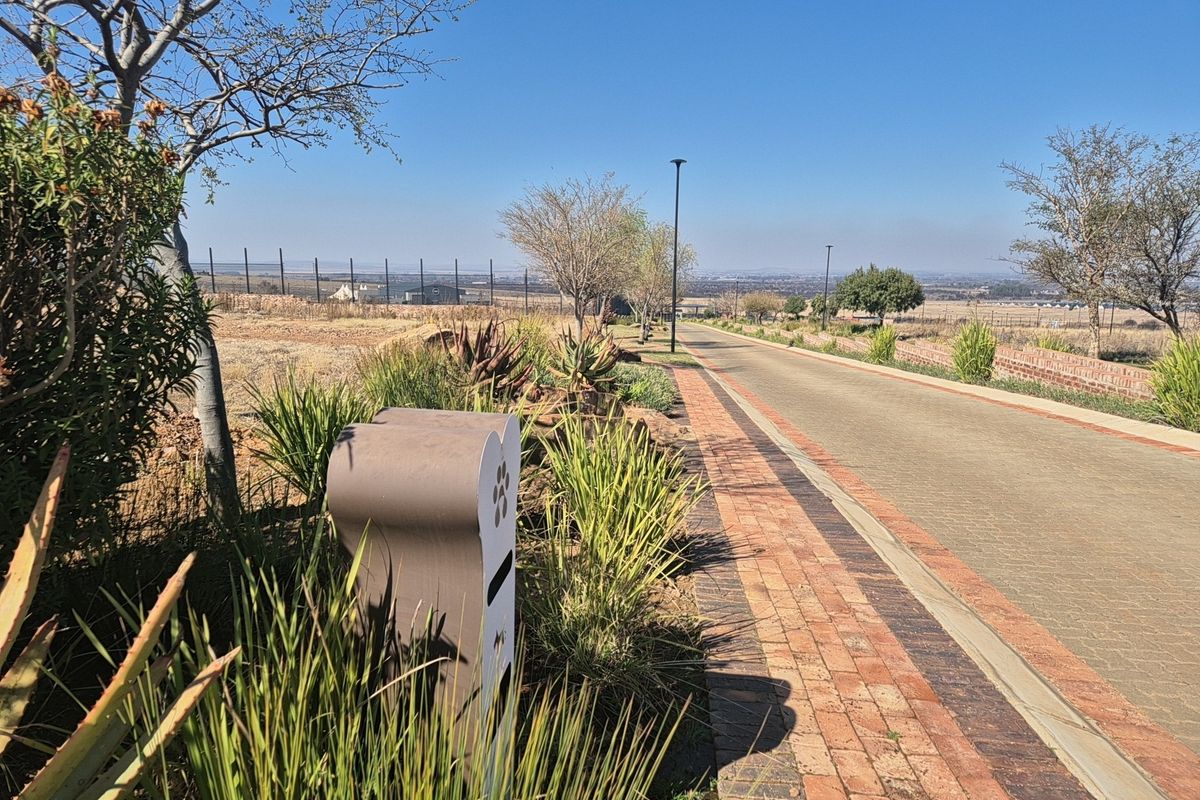 A view of a paved residential street with brick edging, landscaped verges, and perimeter fencing in a well-maintained estate setting.