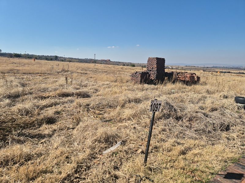 A view of a vacant residential plot featuring dry grass and a property boundary marker, suitable for future development.