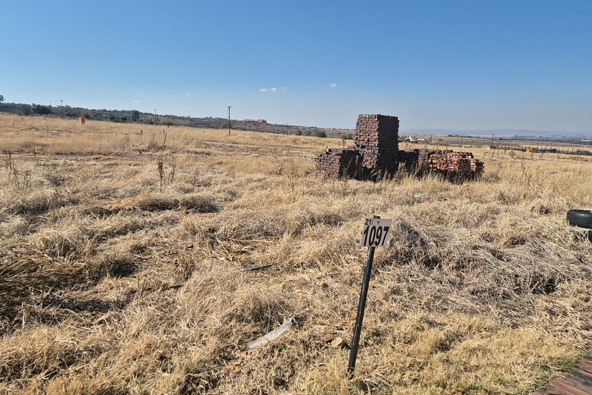 A view of a vacant residential plot featuring dry grass and a property boundary marker, suitable for future development.