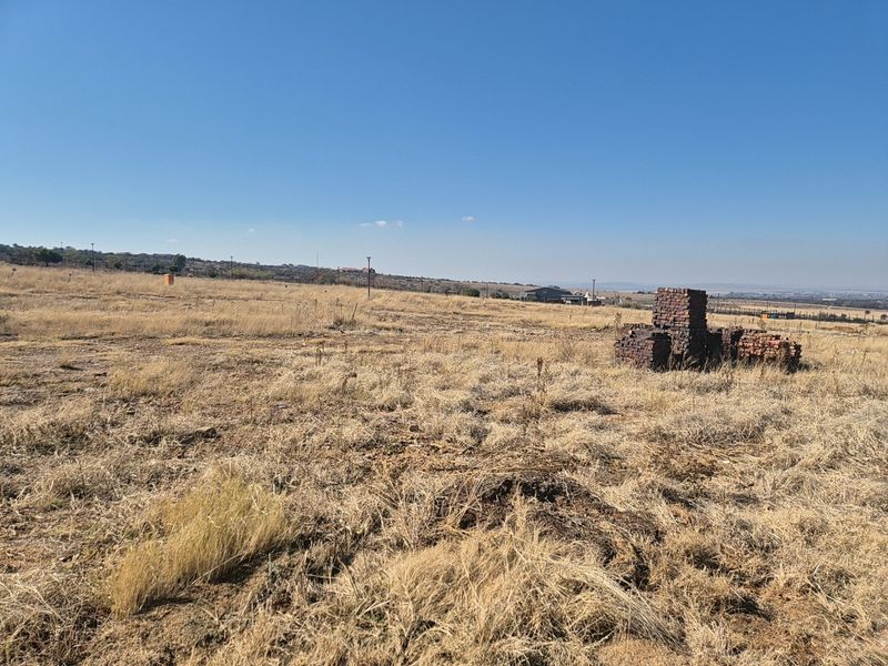A wide-angle view of a vacant residential plot featuring dry grass, perimeter fencing, and utility infrastructure, offering a clear perspective of the land.