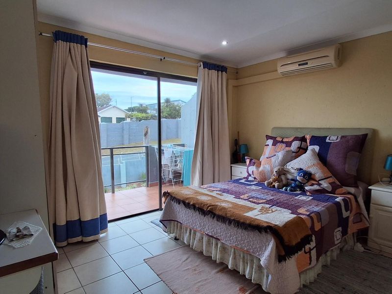 A bedroom featuring tiled flooring, a wall-mounted air conditioning unit, and sliding glass doors that open onto a private balcony.