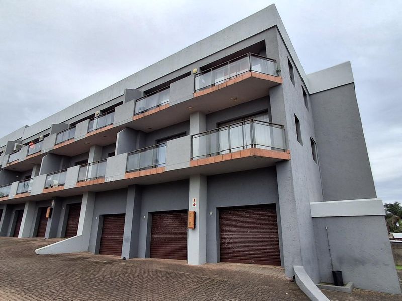 Modern multi-story apartment complex featuring grey facade, integrated ground-level roller shutter garages, and private balconies with glass balustrades.