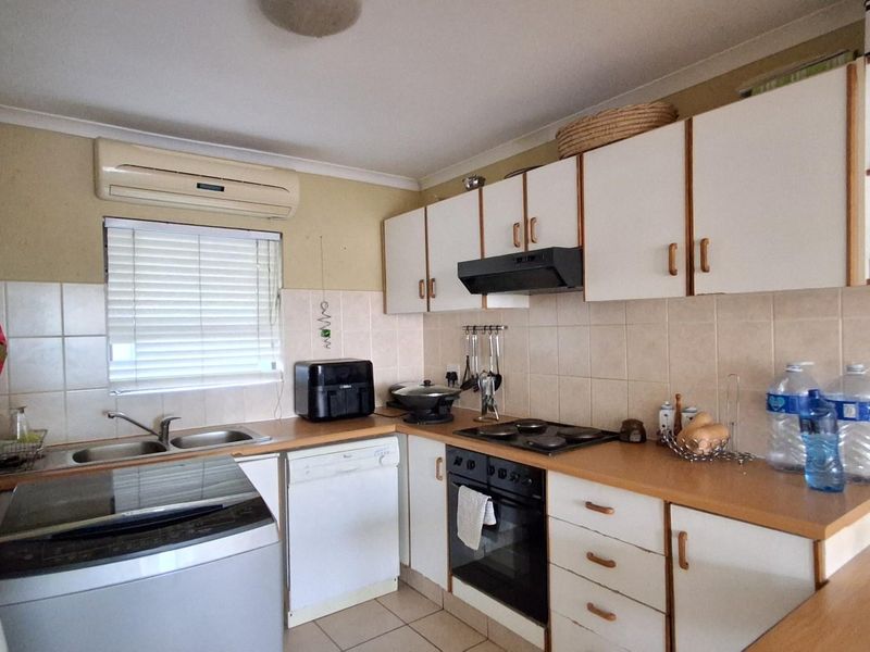 Functional kitchen featuring built-in cabinetry, integrated oven, hob, extractor fan, double sink, and wall-mounted air conditioning unit.