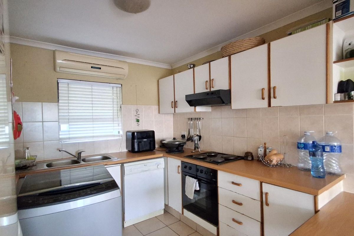 Functional kitchen featuring built-in cabinetry, integrated oven, hob, extractor fan, double sink, and wall-mounted air conditioning unit.