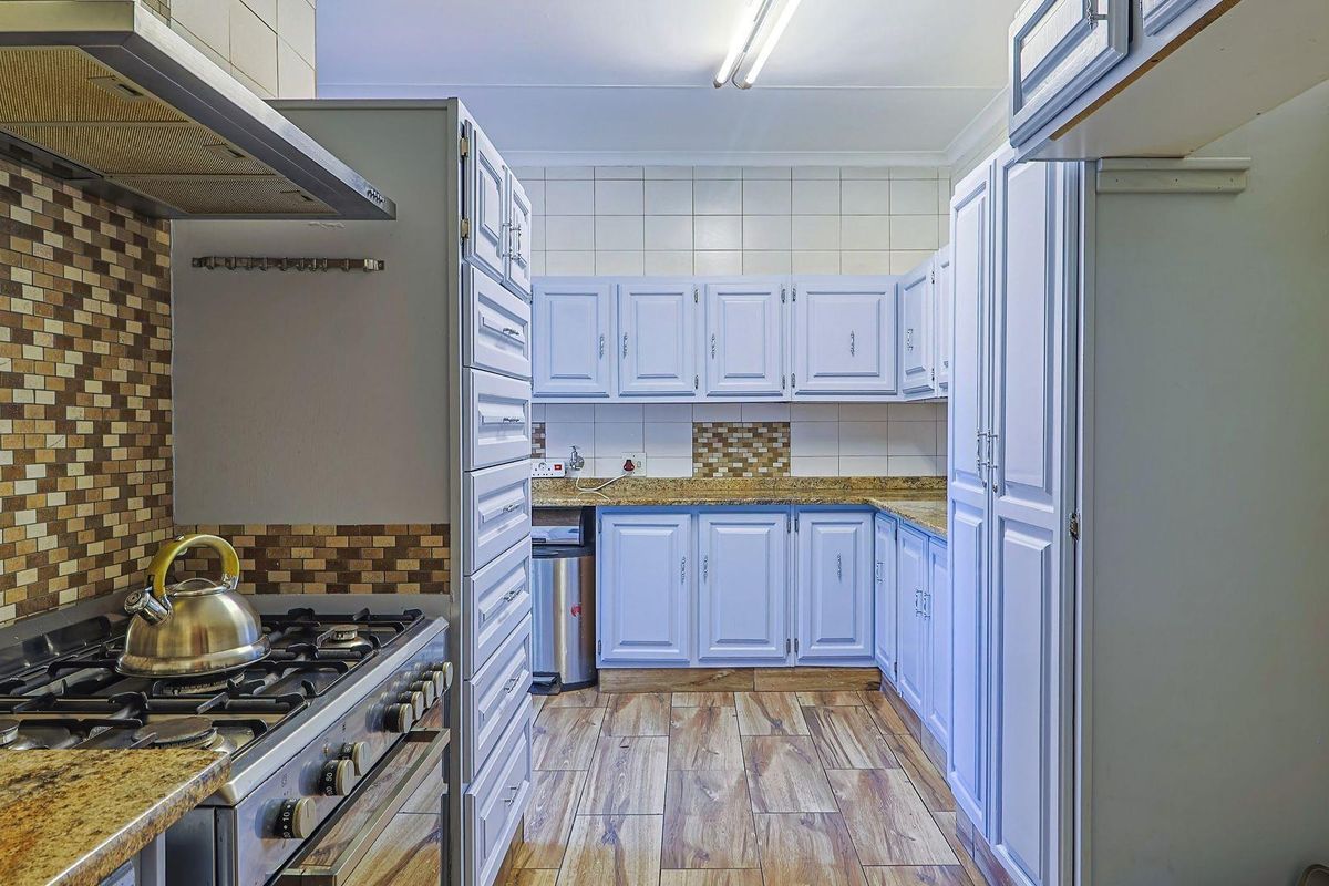 A functional kitchen featuring light-colored cabinetry, granite countertops, mosaic tile backsplash, and wood-look floor tiles with a built-in gas stove.