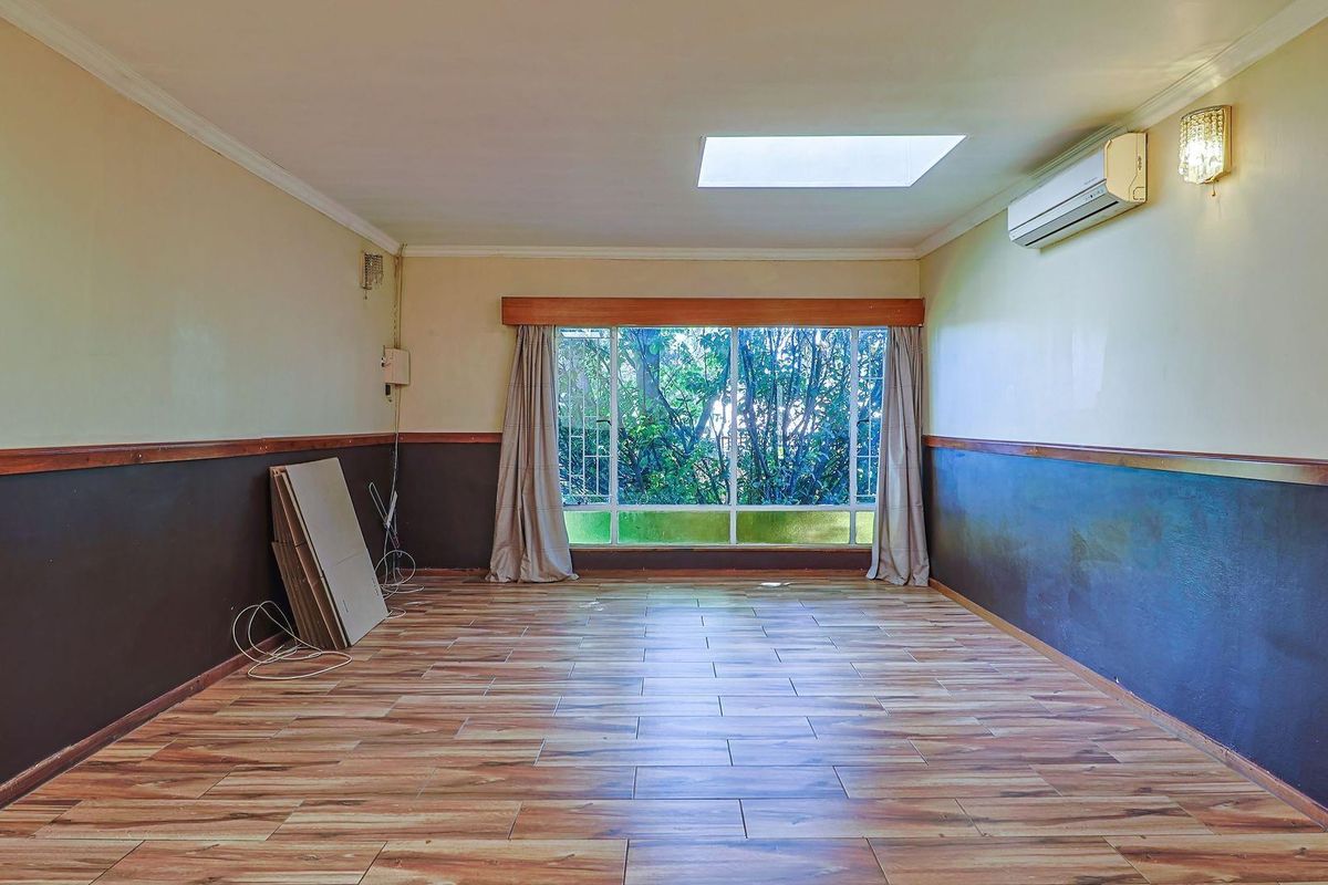 Spacious living area featuring wood-look tile flooring, a large window with garden views, a skylight, and a wall-mounted air conditioning unit.