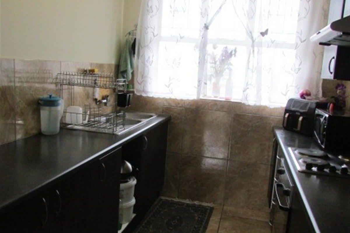 A functional galley-style kitchen featuring dark cabinetry, tiled splashbacks, a built-in hob, and an integrated sink area with natural light.
