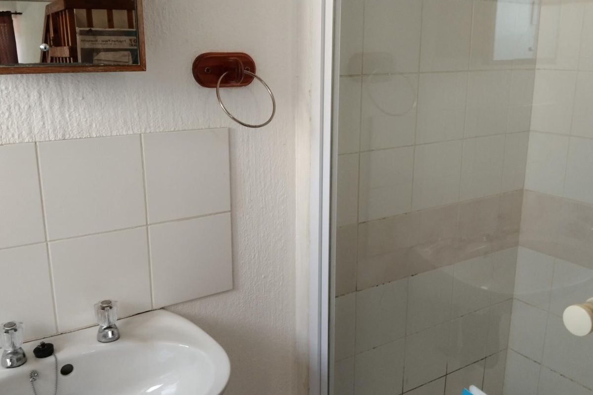 A functional bathroom featuring a wall-mounted basin with chrome taps and a tiled shower enclosure with a glass door.